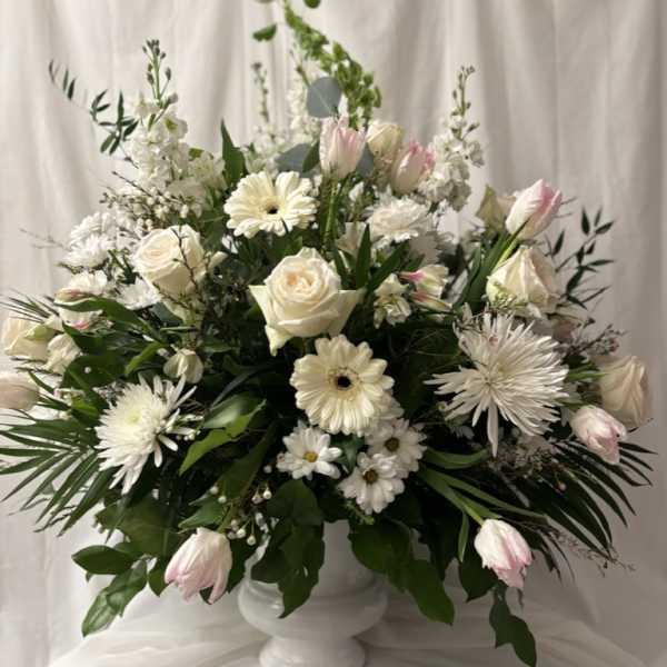 White floral arrangement in a white pedestal vase with pink tulips and roses