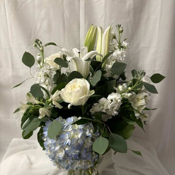 White lilies, roses, and blue hydrangea in a glass vase