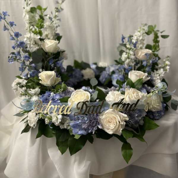 Floral wreath with white roses, blue flowers, and a gold "Beloved Dad" sign