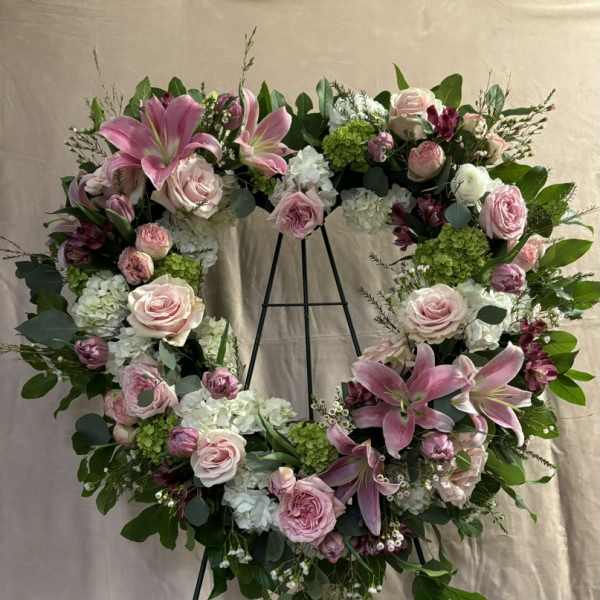 Heart-shaped floral wreath with pink lilies and roses on a black stand