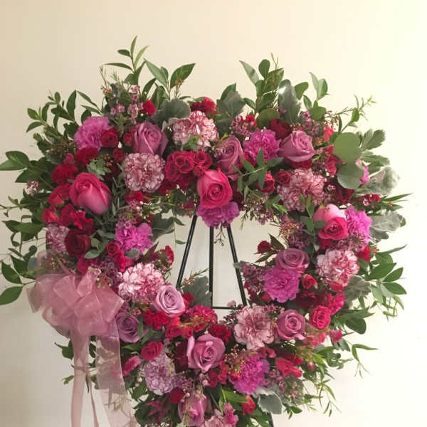 Heart-shaped floral wreath with pink and red roses on a stand