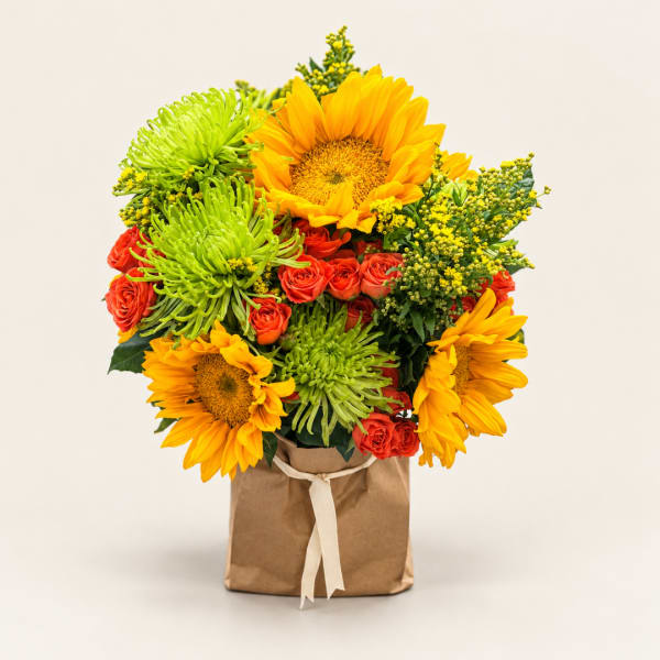 Bouquet of sunflowers, green spider mums, and red roses in a paper bag