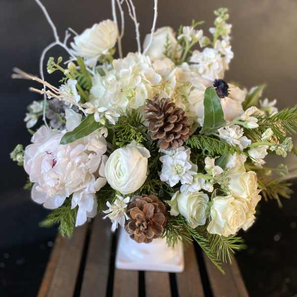 White floral arrangement with pinecones in a white container