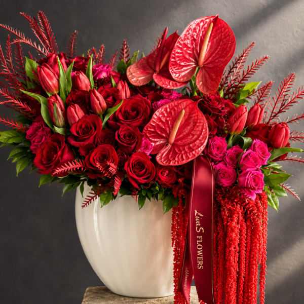 Red roses and anthuriums in a white vase with a burgundy ribbon