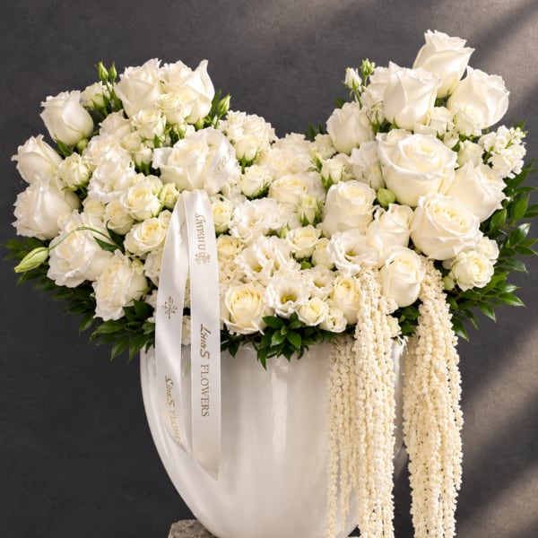 White rose arrangement in a white vase with trailing cream flowers