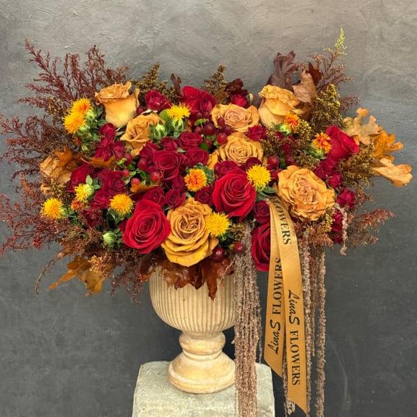 Large bouquet of red and gold roses in a cream urn vase with autumn foliage