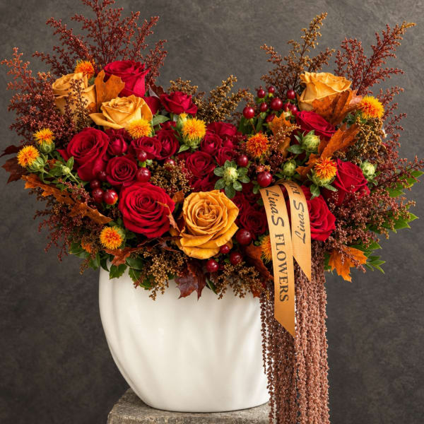 Red and gold rose arrangement in a white vase with autumn leaves