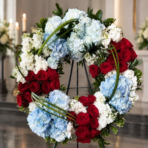 Heart-shaped wreath of red roses, blue and white hydrangeas, and white flowers on a stand