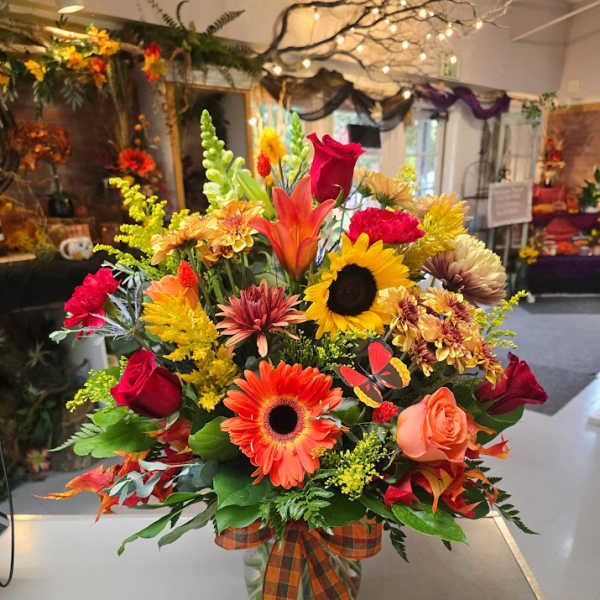 Autumn bouquet with sunflowers, roses, and gerbera daisies in a glass vase