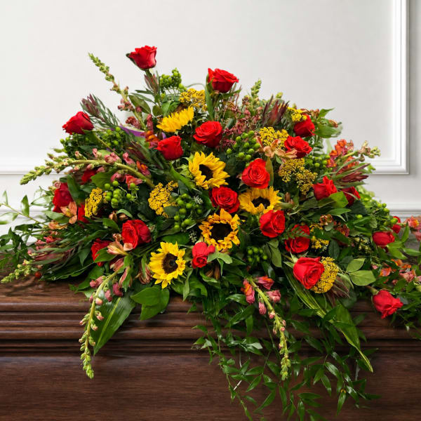 Large arrangement of red roses and yellow sunflowers on a wooden casket