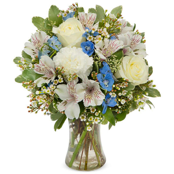 White roses and blue flowers arranged in a clear glass vase