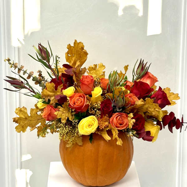 Autumn floral arrangement in a pumpkin vase with red, orange, and yellow roses