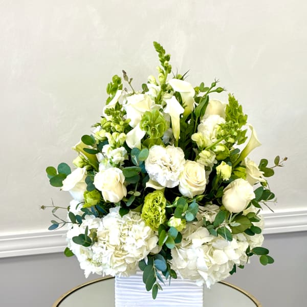 White floral arrangement in a ribbed white vase with green accents