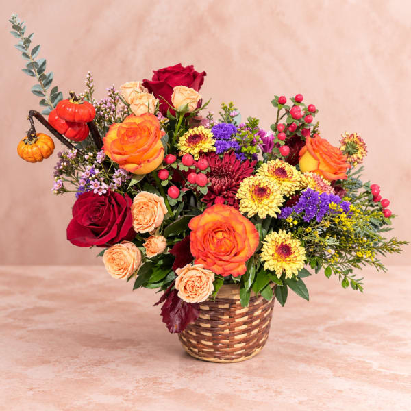 Basket arrangement of roses, chrysanthemums, and berries with small pumpkins