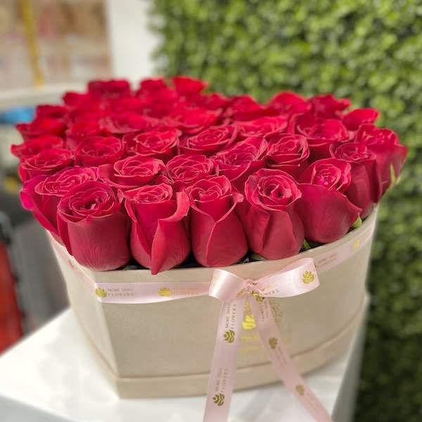 Box of red roses arranged tightly in a beige hat box with a pink ribbon bow