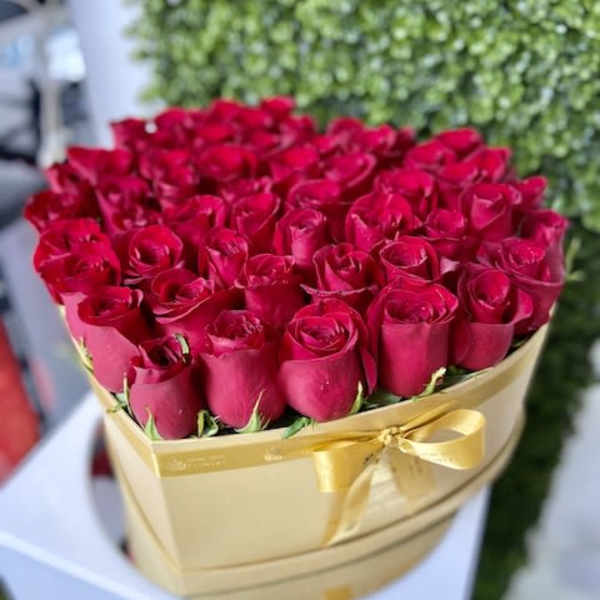 Heart-shaped gold box filled with red roses and tied with a gold ribbon