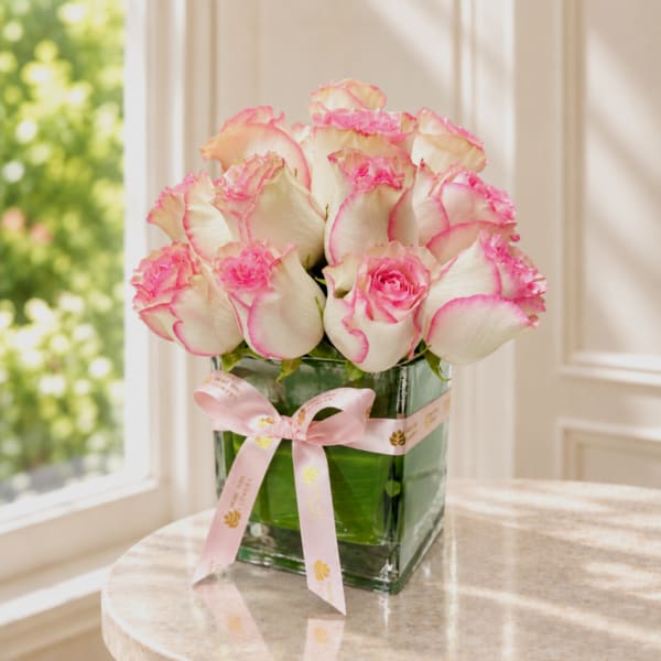 Pink-edged white roses in a square glass vase with a pink ribbon