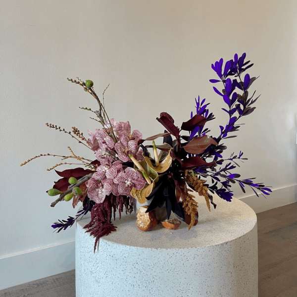 Purple and pink floral arrangement in a low vase on a round pedestal