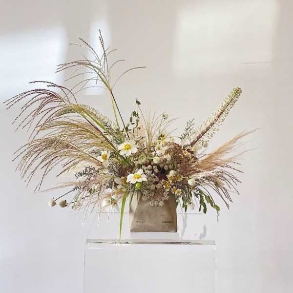 Wildflower arrangement with white daisies and tall grasses in a neutral vase