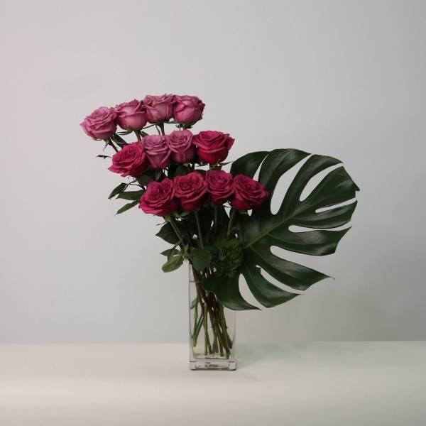 Pink roses in a clear rectangular vase with a large tropical leaf
