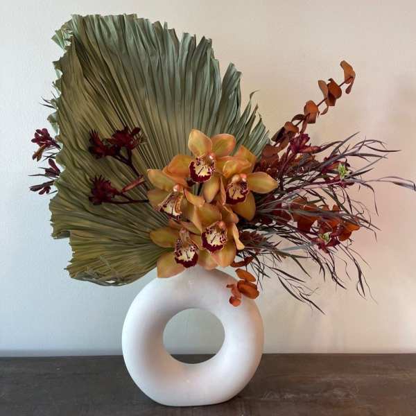 Orchid arrangement with a large fan-shaped leaf in a white ring vase