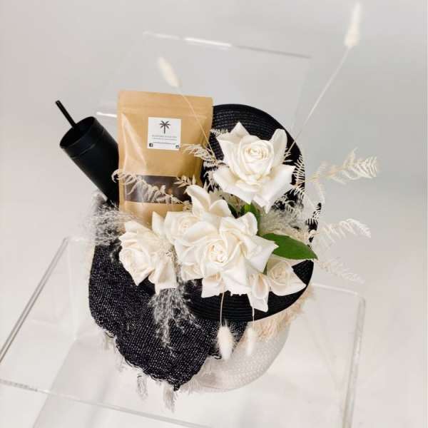 White roses arranged with a black tumbler and packaged gift bag