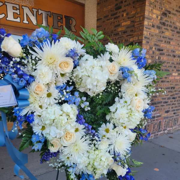 Heart-shaped floral wreath with white and blue flowers on a stand