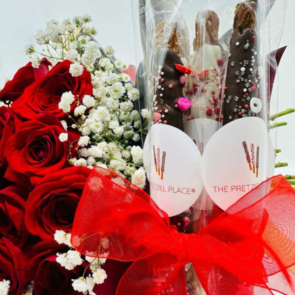 Red roses with white baby's breath beside chocolate-covered pretzels in a clear wrap