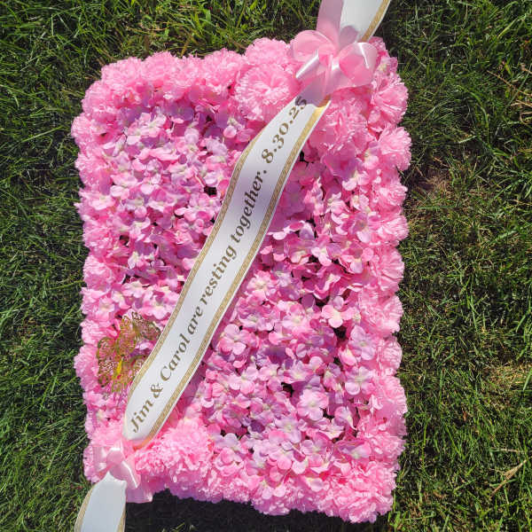 Pink floral sympathy pillow with ribbon sash on grass