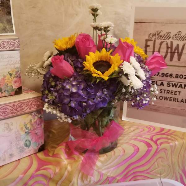 Bouquet of pink roses, sunflowers, and purple hydrangeas in a glass vase