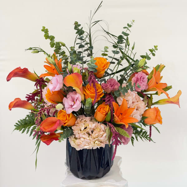 Orange roses and calla lilies in a black vase with pink blooms