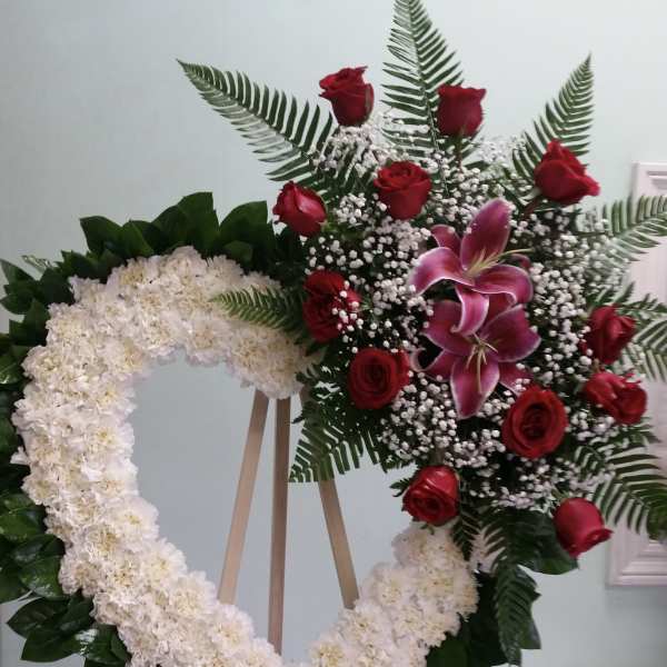 Heart-shaped floral wreath with red roses and white flowers on an easel