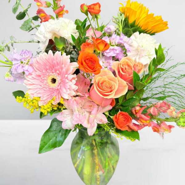 Mixed bouquet of pink, orange, yellow, and white flowers in a glass vase