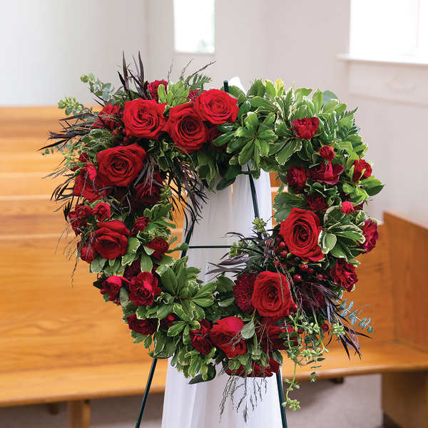 Heart-shaped red rose wreath on a stand with greenery