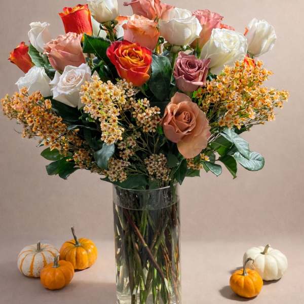 Mixed roses in a clear glass vase with small pumpkins around it