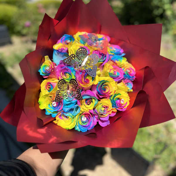 Rainbow bouquet of roses wrapped in burgundy paper with butterfly picks