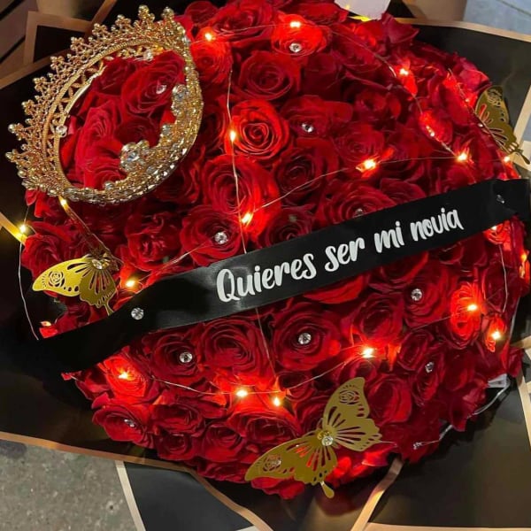 Red rose bouquet with a jeweled crown and a black ribbon reading "Quieres ser mi novia"