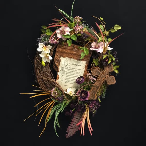 Floral wreath with a prayer card and mixed blooms on a dark background