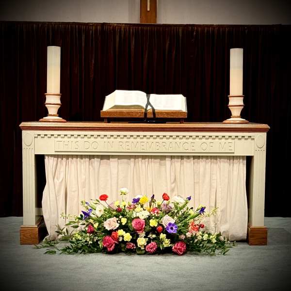 Colorful mixed floral spray with roses and other blooms arranged at the base of a church altar table