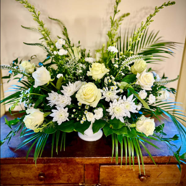 Low white and cream flower arrangement with roses and mums accented by tall palm fronds in a white bowl