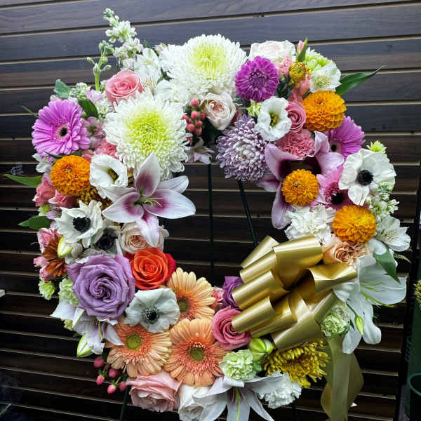 Heart-shaped floral wreath with mixed blooms and a gold ribbon bow