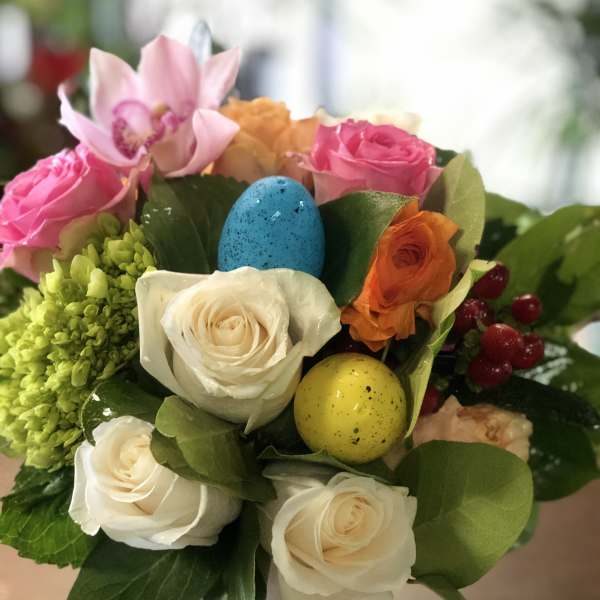 Colorful arrangement of roses, hydrangea, and orchid with speckled eggs in a small ceramic vase