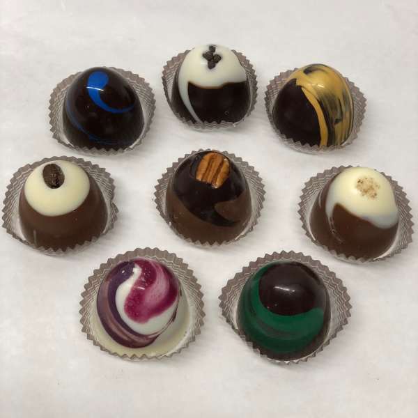 Assortment of eight decorated round chocolate truffles in paper cups on a white surface