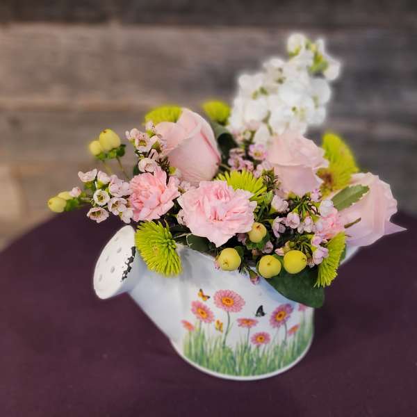Low arrangement of pink roses and carnations with white blooms in a painted watering can.