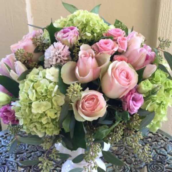 Round arrangement of pink roses and green hydrangeas in a white pedestal vase