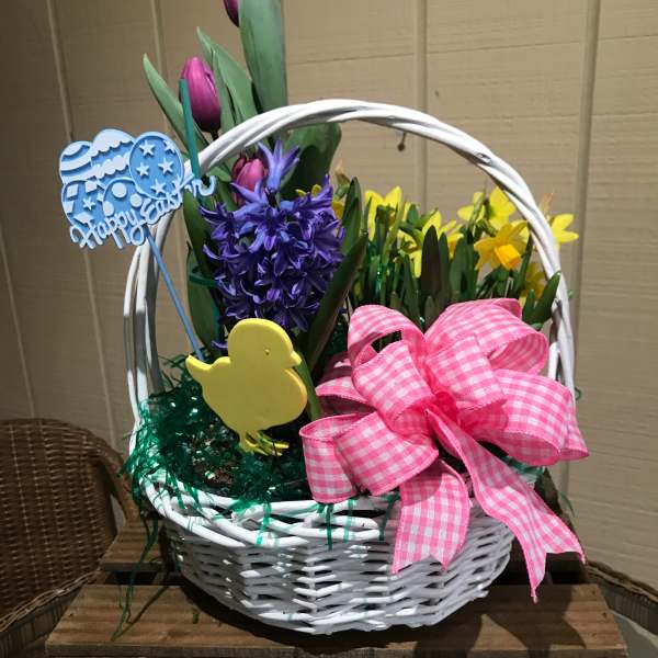 Easter basket of purple tulips, hyacinth, and yellow daffodils with a pink bow and festive decorations.
