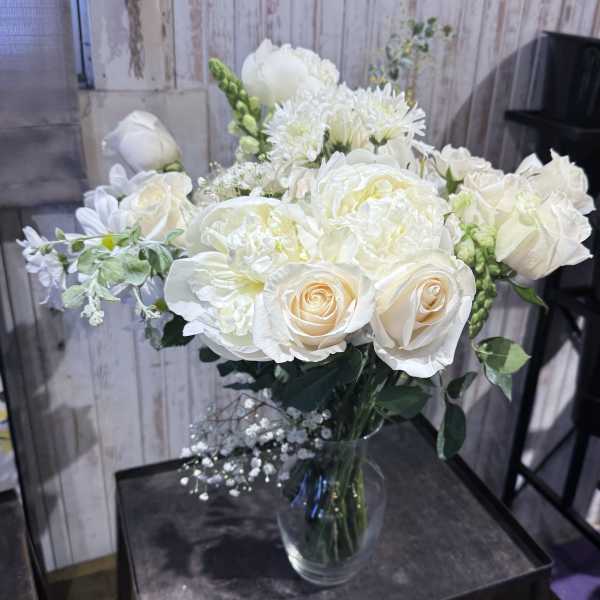 Ivory and cream roses with mixed white flowers arranged in a clear glass vase