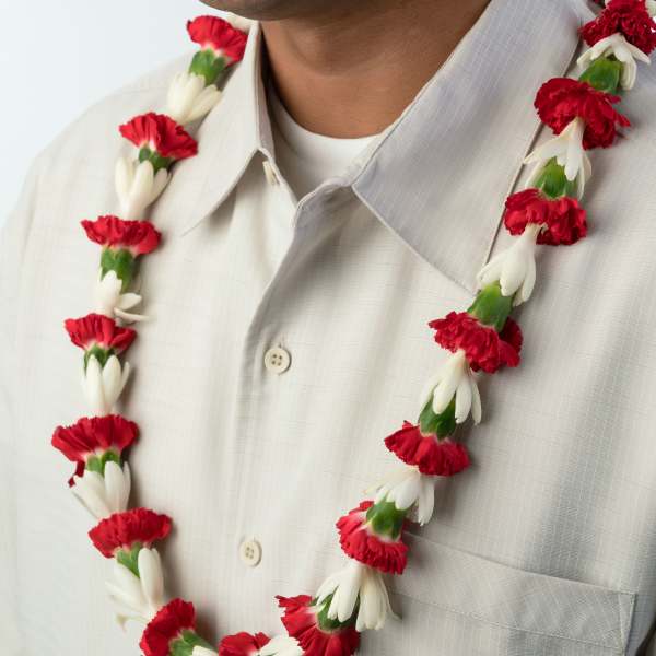 Red and white flower lei worn around a person’s neck over a light collared shirt