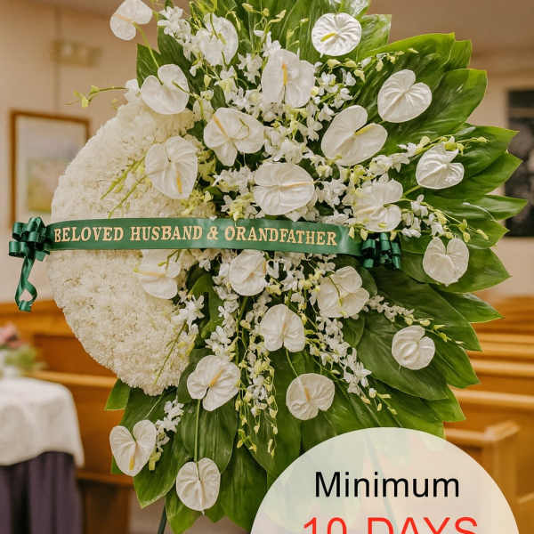 Tall white sympathy standing spray with clustered white flowers and glossy green leaves on an easel.