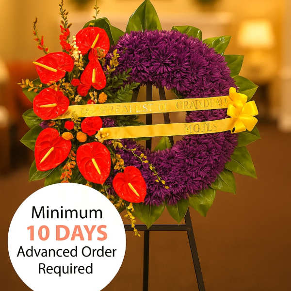 Standing purple wreath with red tropical flowers, yellow ribbon, and bow on a black easel.
